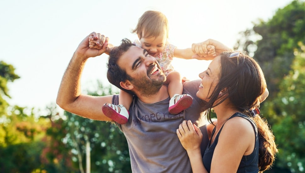 Father with wife holding toddler on his shoulders.