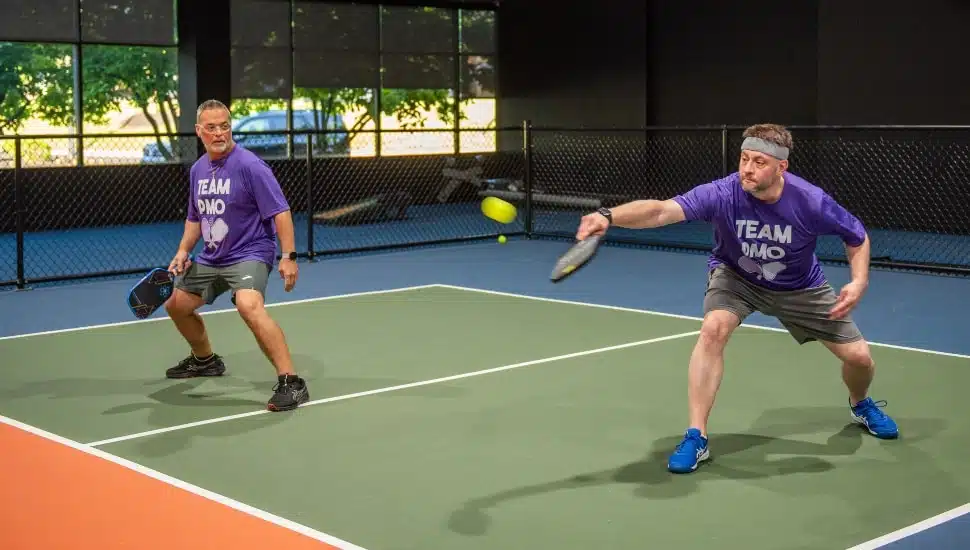 Two middle-aged men in purple shirts play pickleball.
